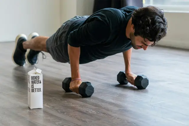 Hombre haciendo flexiones apoyado sobre dos mancuernas en un suelo de madera