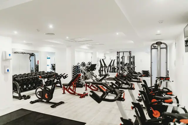 Sala luminosa con máquinas de musculación, bicicletas estáticas y soportes de discos